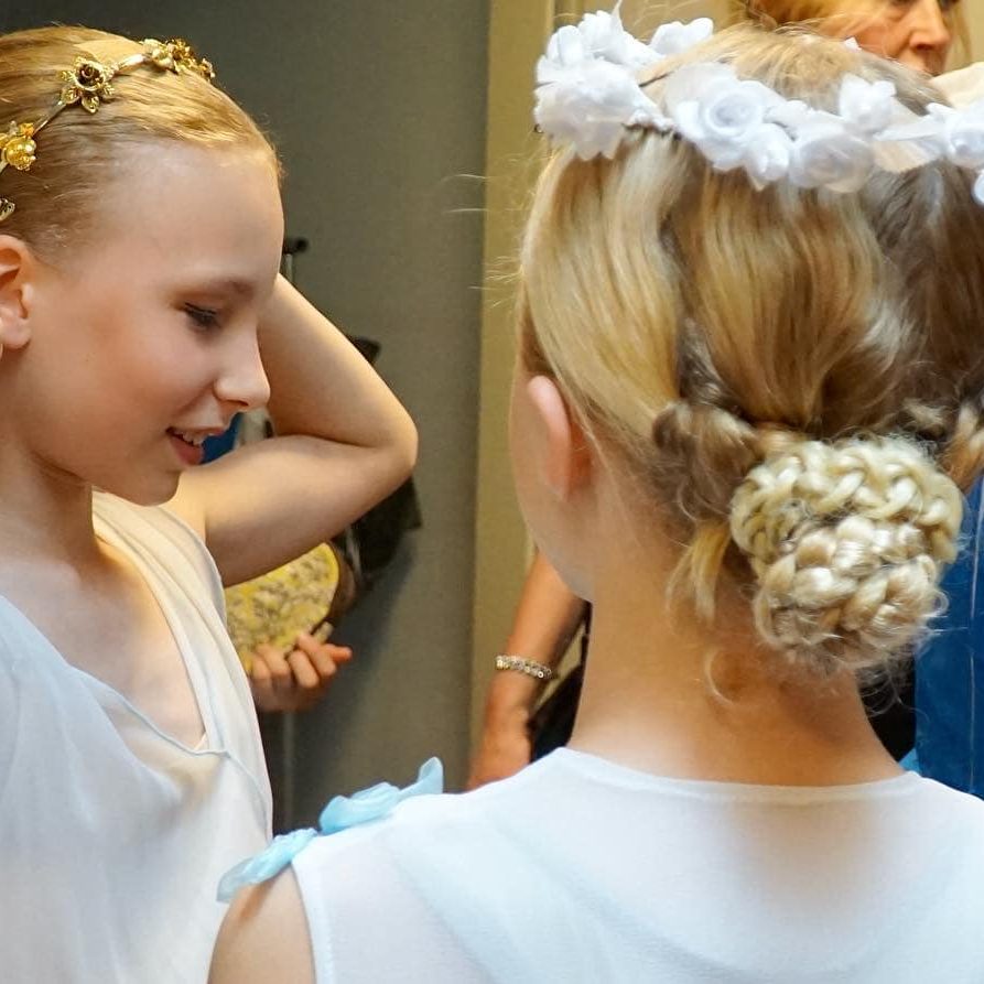 Ein Mädchen steht mit dem Rücken begutachtet sich in Ihrem blauen Kostüm und zupft an Ihrem Blumenkranz auf dem Kopf.