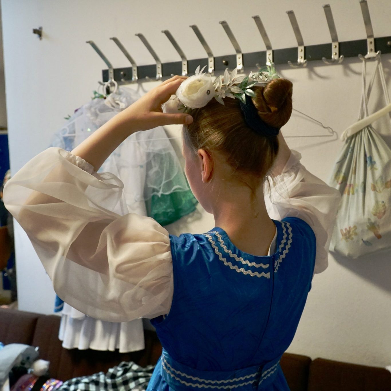 Ein Mädchen steht mit dem Rücken begutachtet sich in Ihrem blauen Kostüm und zupft an Ihrem Blumenkranz auf dem Kopf.